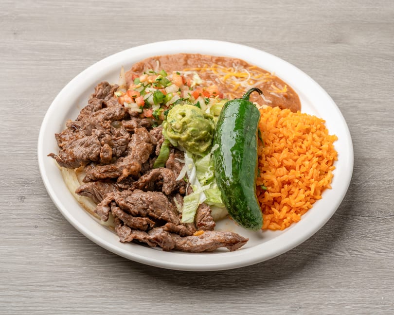 Carne asada plate with rice, refried beans, guacamole, pico de gallo, and a whole jalapeño.