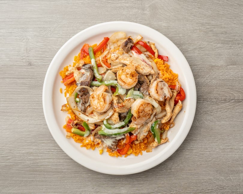 A white plate of orange rice topped with shrimp, chicken, steak, and vegetables in a creamy sauce.