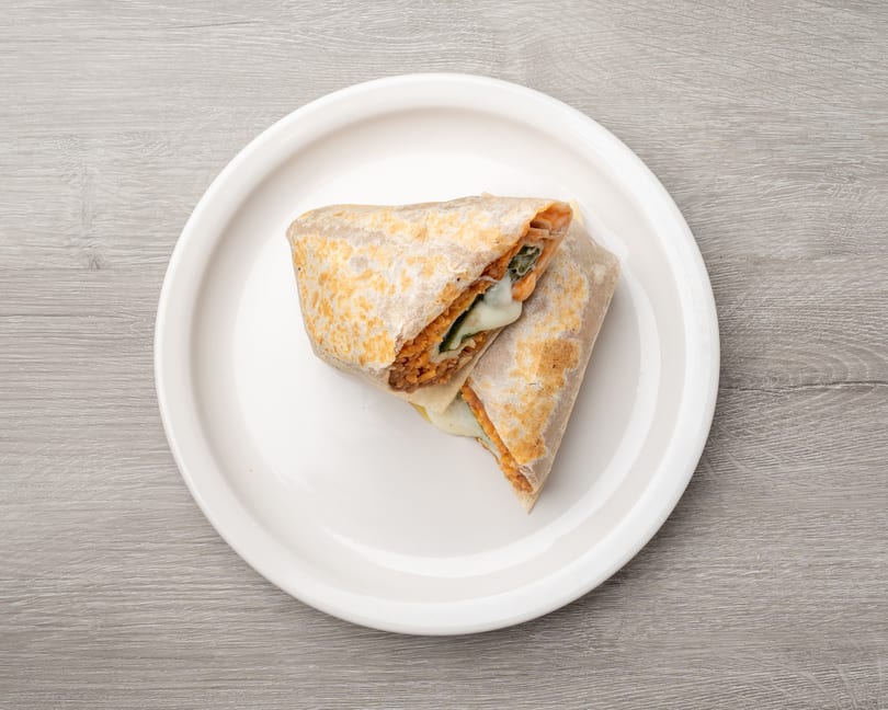 Two halves of a burrito, filled with orange rice, green vegetables, and melted cheese, on a white plate.