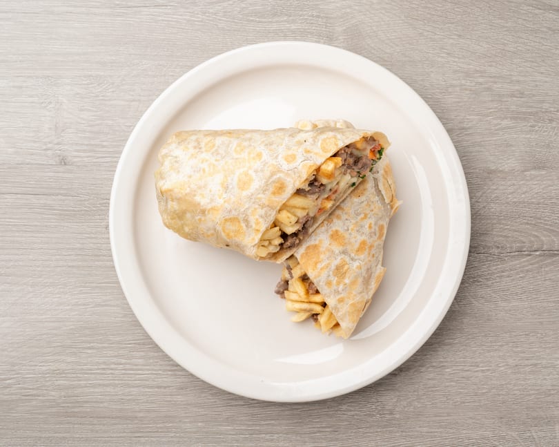 Two halves of a burrito filled with meat, cheese, and french fries on a white plate.