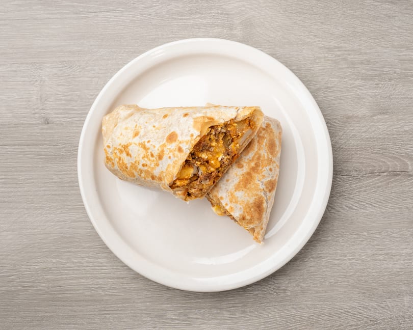 A large breakfast burrito, cut in half, revealing eggs, potatoes, and chorizo on a white plate.