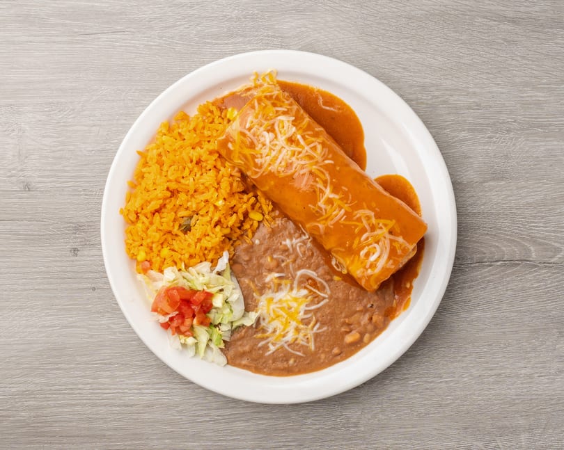 A burrito covered in red sauce and cheese, with rice, refried beans, and salad on a white plate.