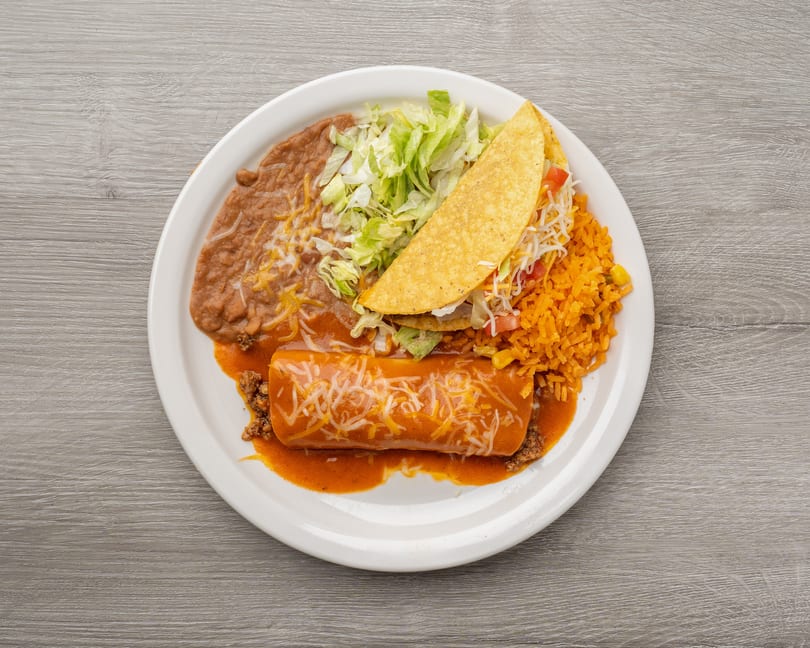 A white plate holds a burrito, taco, refried beans, rice, and shredded lettuce.